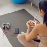 Femeie consumă un bol cu cereale și fructe înainte sau după antrenament, alături de echipament de fitness.