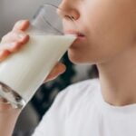 Prim-plan cu o femeie care bea un pahar cu lapte proaspăt, ca parte a unei alimentații echilibrate.