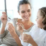 Mamă și fiică savurează împreună iaurt natural, într-un moment de familie care evidențiază beneficiile unui mic dejun sănătos.