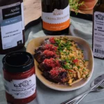 O portie de aripioare de pui caramelizate Fragedo cu o sticla de vin in fundal