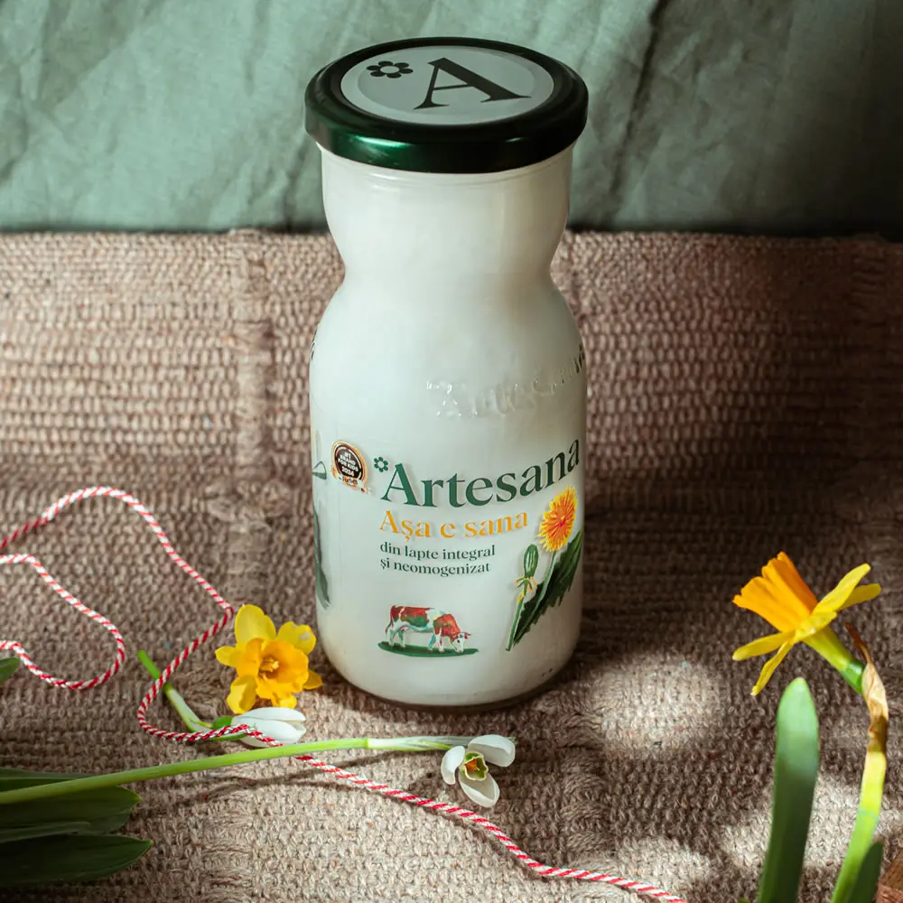 O sticla de sana Artesana langa flori si un martisor