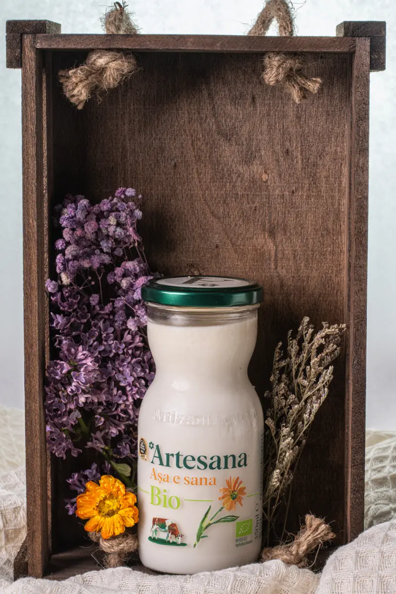 Sticlă de sana ecologică Artesana Bio, realizată din lapte românesc certificat ecologic, prezentată într-o cutie decorată cu flori uscate.