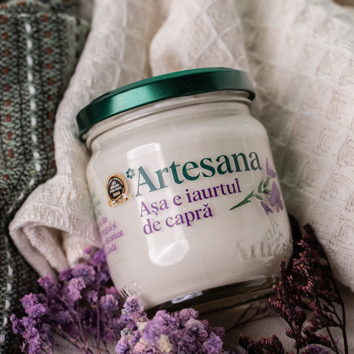 Iaurt natural de capra Artesana la 160g pe o masa langa flori de camp mov uscate