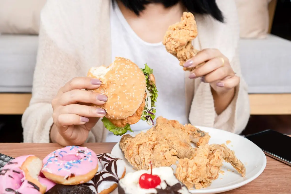 Femeie consumând alimente ultraprocesate în exces (burger, carne prăjită, gogoși) 