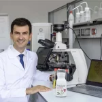 Prof Dan C Vodnar în laboratorul USAMV Cluj-Napoca analizând un produs lactat Artesana, lângă un microscop și un laptop cu imagine microscopică pe ecran