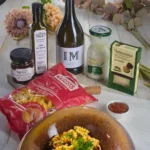 O salata de paste cu piept de pui, un borcan cu rosii uscate, o sticla de ulei de nuca, o sticla de vin Chardonay, o sticla de sana Artesa, o punga de paste Monte Banato si o cutie cu branza maturata cu trufe negre de la Artesana