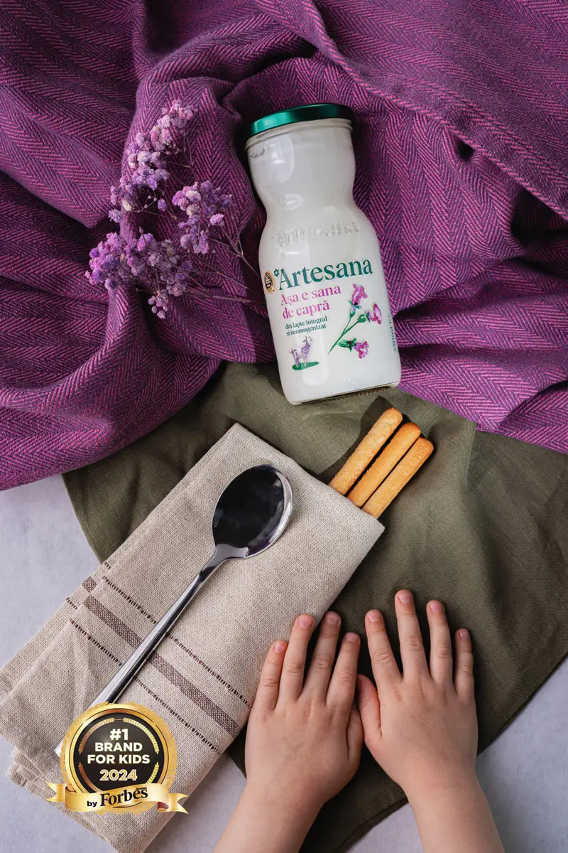 o sticla de kefir de capra artesana la 350ml, pe un fundal textil mov, cu doua maini de copil in dreapta jos si sigla Forbes #1 Brand For Kids in stanga jos