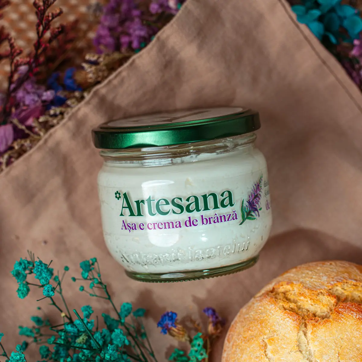 Crema de branza de capra Artesana intr-un borcan de 200g. pe un fundal textil, langa flori de camp si o paine alba