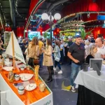 Vizitatori degustând lactate artizanale Artesana într-un spațiu decorat cu roșu și verde, cu lumini ambientale.