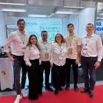 Echipa Artesana formată din Lidia, Laura, Sergiu, Paul, Cristi și Eugene, îmbrăcați în cămăși albe și ecusoane, pozând împreună la standul de prezentare din cadrul unui târg internațional. În fundal se văd afișele brandului și mesajul The way milk is supposed to beL