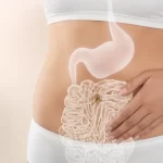 O imagine reprezentând zona abdominală a unei femei, cu o ilustrație suprapusă a stomacului și intestinelor, care evidențiază procesul digestiv și sănătatea tractului gastrointestinal. Mâna așezată pe abdomen sugerează atenție la confort, digestie ușoară și echilibru interior. Fundalul luminos și tonurile calde transmit senzația de calm, sănătate și îngrijire naturală.