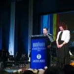 Discurs oficial la Hanukkah Gala 2025, susținut pe scena Operei NATIONALE Bucuresti de Daniel Jinga si Tova Ben Nun-Cherbis eveniment cultural, la pupitrul Laude-Reut, cu decor elegant și orchestră în fundal