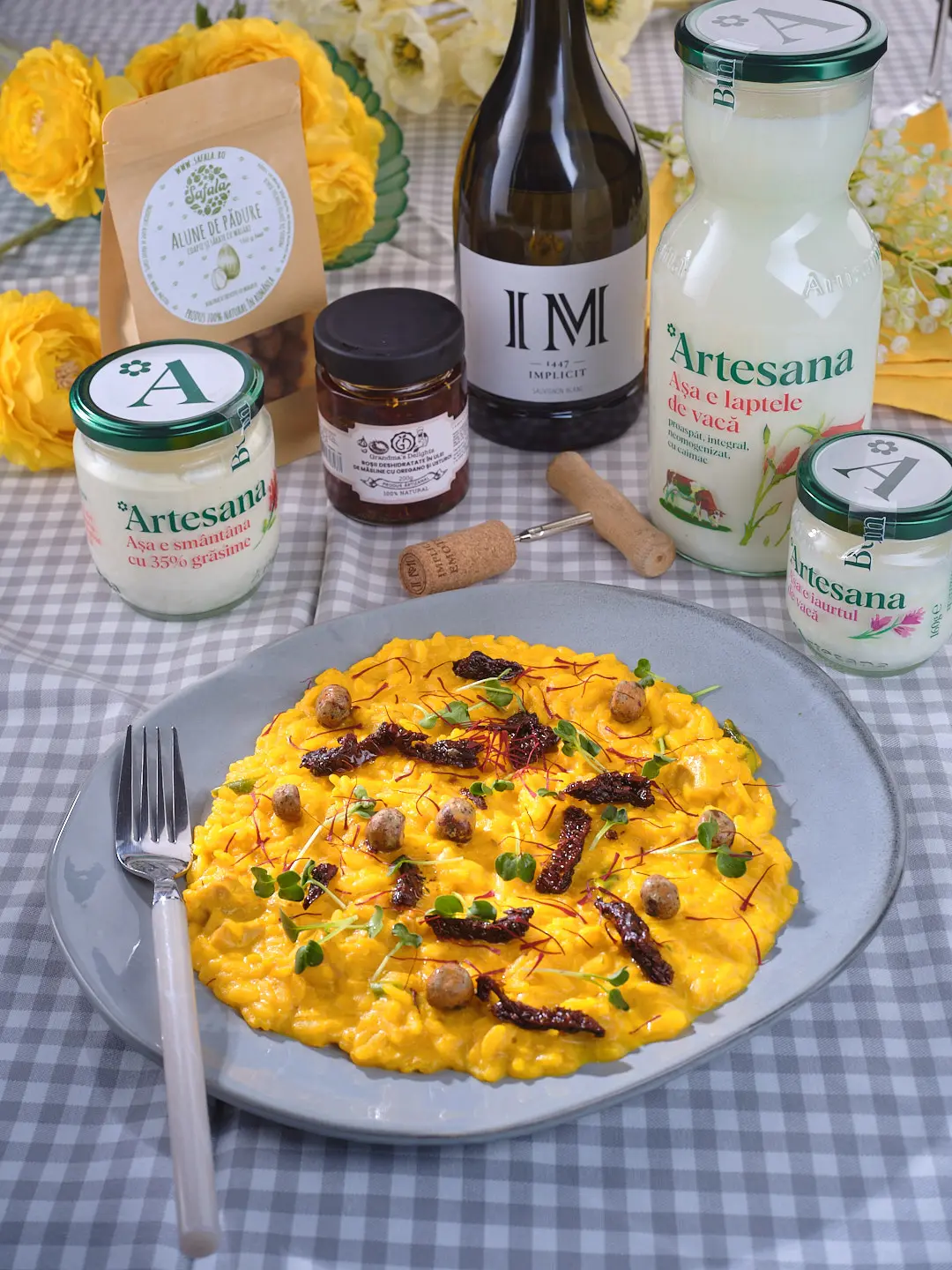 Risotto alla milanese cu infuzie de șofran, servit pe farfurie gri, preparat cu smântână și iaurt Artesana, alături de ingrediente naturale și vin alb pe masă cu față în carouri.