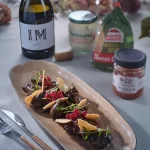 Ficăței de pui gătiți cu smântână aromatizată Artesana, serviți elegant pe platou ceramic, alături de vin roșu și ingrediente gourmet