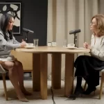Alina Donici și Adina Alberts în timpul unui podcast, așezate față în față la o masă rotundă, cu microfoane profesionale și cești de cafea, într-un studio elegant.
