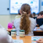 Două borcane de iaurt Bio Artesana pe banca unei săli de clasă, în timpul orei, parte din pachețelul pentru școală al elevilor.
