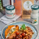 Pulpe de pui marinate în sana Artesana și rumenite la cuptor, servite cu cartof dulce copt, roșii cherry caramelizate și alune de pădure, alături de smântână 35% grăsime și sana Artesana, ingrediente naturale pentru o rețetă savuroasă.