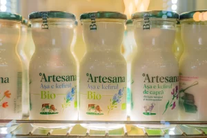 Sticle de chefir Artesana Bio și chefir de capră expuse în vitrină frigorifică, evidențiind produse lactate artizanale din lapte integral la stand expozițional.