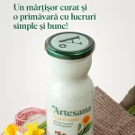Sticlă de lapte Artesana „Așa e sana”, din lapte integral și neomogenizat, cu capac verde, așezată pe material textil, alături de flori galbene de primăvară și șnur de mărțișor, mesaj „Un mărțișor curat și o primăvară cu lucruri simple și bune”.