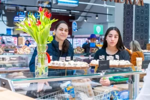 Atelier Artesana de 8 Martie într-un supermarket – degustare de brânzeturi artizanale din lapte de capră și vacă, cu participanți și stand decorat cu flori