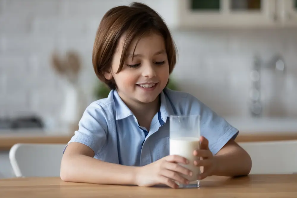 Copil fericit bând un pahar de lapte la masă, alimentație sănătoasă pentru copii, consum de produse lactate naturale