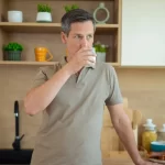 Bărbat adult bea un pahar de lapte în bucătărie modernă, atmosferă casnică, consum de produse lactate sănătoase