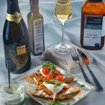 Bruschete gourmet cu cremă de brânză Artesana cu mărar, piept de pui fraged în stil oriental cu ciuperci shimeji, ou poșat și roșii cherry, servite alături de vin spumant și ingrediente premium.