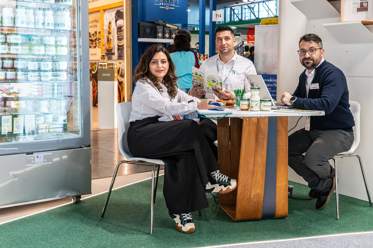 Lidia Mulțescu, Călin Sergiu Cuc și Iulian Donici reprezintă Artesana la târgul internațional Tutto Food Milano 2026, într-un stand cu produse lactate artizanale expuse.