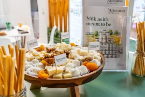 Platou cu brânzeturi Artesana și gustări artizanale prezentate la standul brandului în cadrul târgului Tutto Food Milano 2026, alături de materiale de promovare și produse lactate.