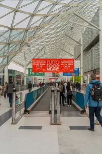 Panou oficial Tutto Food Milano 2026 amplasat la intrarea în complexul expozițional, unde vizitatorii și expozanții se îndreaptă către halele târgului internațional alimentar.