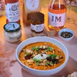 Supă cremă de roșii cu pulpă de pui fragedă, alune de pădure și chili, servită cu cremă de brânză Artesana cu roșii uscate și busuioc, alături de vin rose și produse artizanale gourmet.