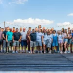 Echipa Artesana la team building, fotografie de grup cu fondatorii și colegii companiei pe o terasă în aer liber, în fața munților, simbol al spiritului de echipă și al producătorului român de lactate artizanale.
