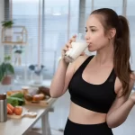 Tânără activă consumând un pahar cu lapte și ținând un măr proaspăt, într-un context de alimentație echilibrată și stil de viață sănătos, evidențiind beneficiile laptelui natural pentru energie, nutriție și recuperare după sport.