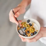 Bol cu iaurt natural Artesana, granola, afine și kiwi, pregătit ca mic dejun bogat în proteine, într-o combinație sănătoasă și echilibrată.