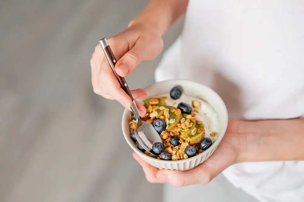 Bol cu iaurt natural Artesana, granola, afine și kiwi, pregătit ca mic dejun bogat în proteine, într-o combinație sănătoasă și echilibrată.