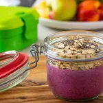 Borcan cu overnight oats preparat din iaurt, fulgi de ovăz, semințe de chia și fructe de pădure, ideal ca mic dejun la pachet pentru birou.