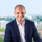 Portret profesional al noului Chief Growth Officer Artesana, Razvan Orbulescu, îmbrăcat în costum bleumarin, cu un peisaj urban în fundal.