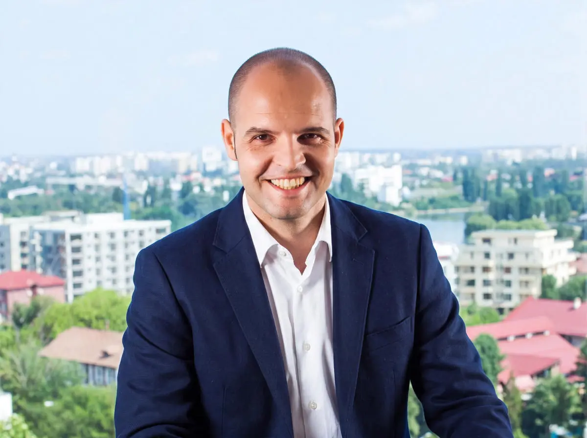 Portret profesional al noului Chief Growth Officer Artesana, Razvan Orbulescu, îmbrăcat în costum bleumarin, cu un peisaj urban în fundal.