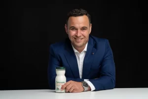 Portret corporate cu Sergiu Mulțescu - CEO Artesana - alături de o sticlă de sana și kefir Artesana, pe fundal negru.