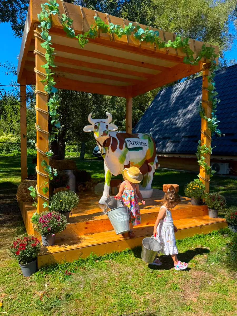 Două fetițe cu găleți, lângă vaca Artesana, în decorul rural amenajat la Family Farm Fest.