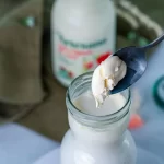 Dop de smântână format natural pe laptele integral, neomogenizat Artesana, ridicat cu lingura din sticla deschisă.