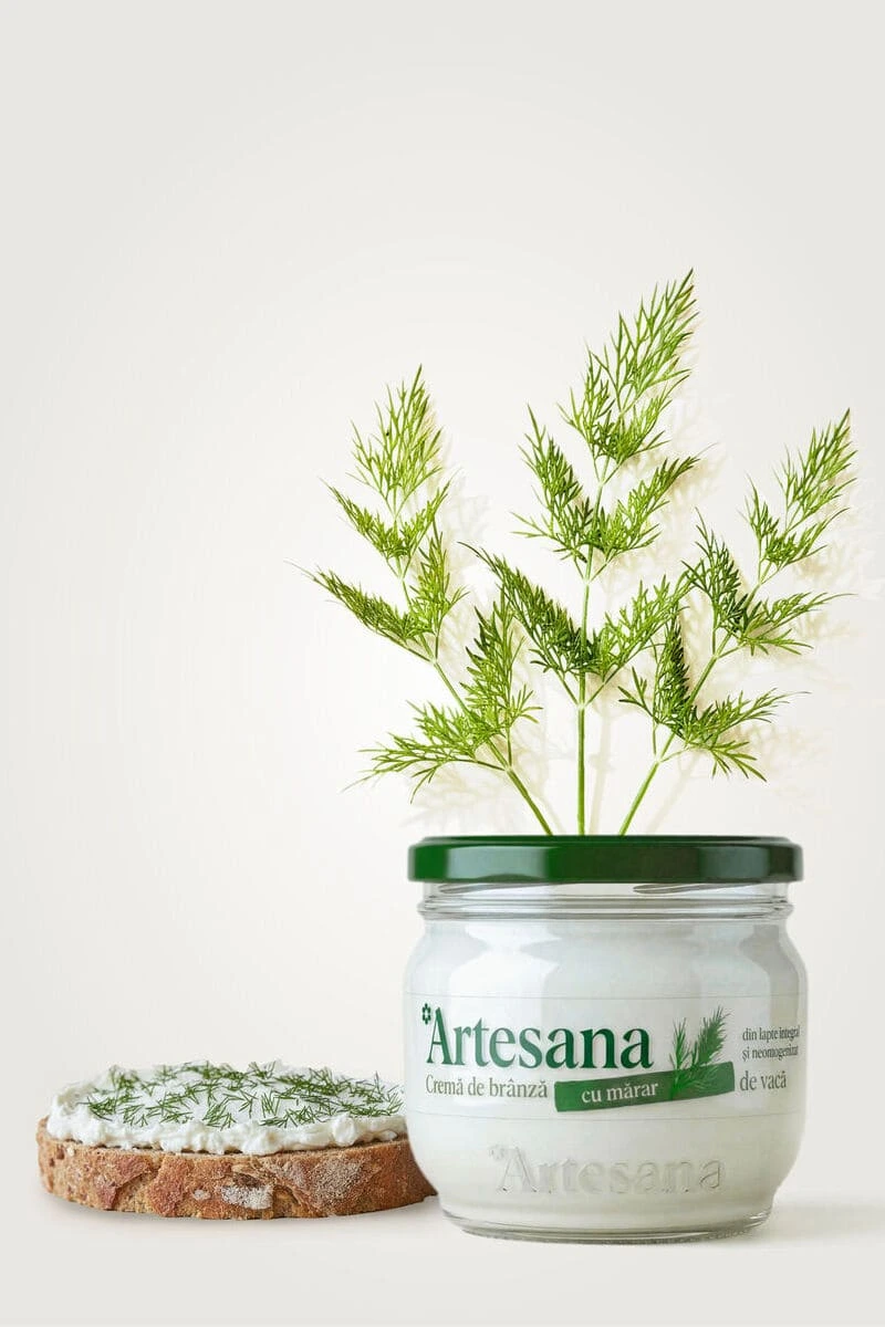 Felie de pâine cu cremă de brânză, lângă borcanul Artesana