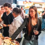 Vizitatoare cu un pahar de vin alege brânzeturi de la cheese barul Artesana, la RO-Wine București 2026.