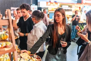 Vizitatoare cu un pahar de vin alege brânzeturi de la cheese barul Artesana, la RO-Wine București 2026.
