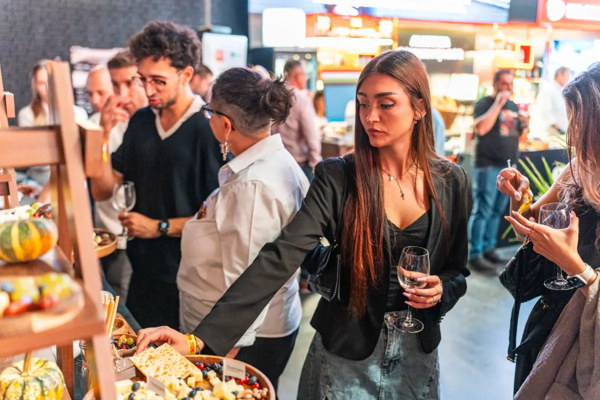 Vizitatoare cu un pahar de vin alege brânzeturi de la cheese barul Artesana, la RO-Wine București 2026.