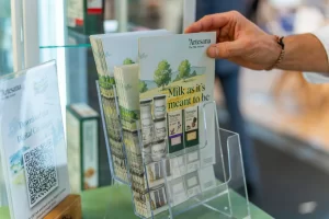 O mână care ia un pliant promoțional Artesana dintr-un suport transparent.