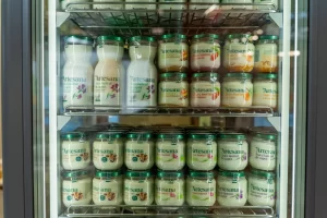 Un frigider de prezentare plin cu borcane de kefir, iaurturi bio, iaurt cu fructe și lapte de capră/Jersey.
