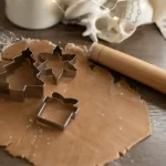 Aluat pentru fursecuri și forme metalice de Crăciun pe blat din lemn.