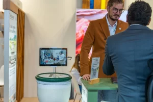 Paul discută cu un vizitator la standul Artesana, lângă un afișaj interactiv.