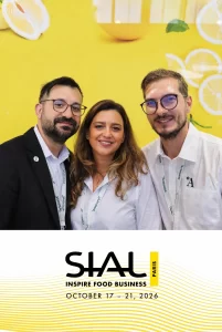 Iulian, Lidia și Paul zâmbesc la o cabină foto personalizată cu logo-ul și grafica evenimentului SIAL Paris 2026.